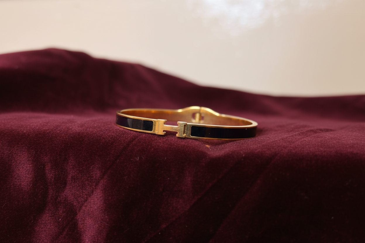 Gold H bangle bracelet on burgundy velvet – front view